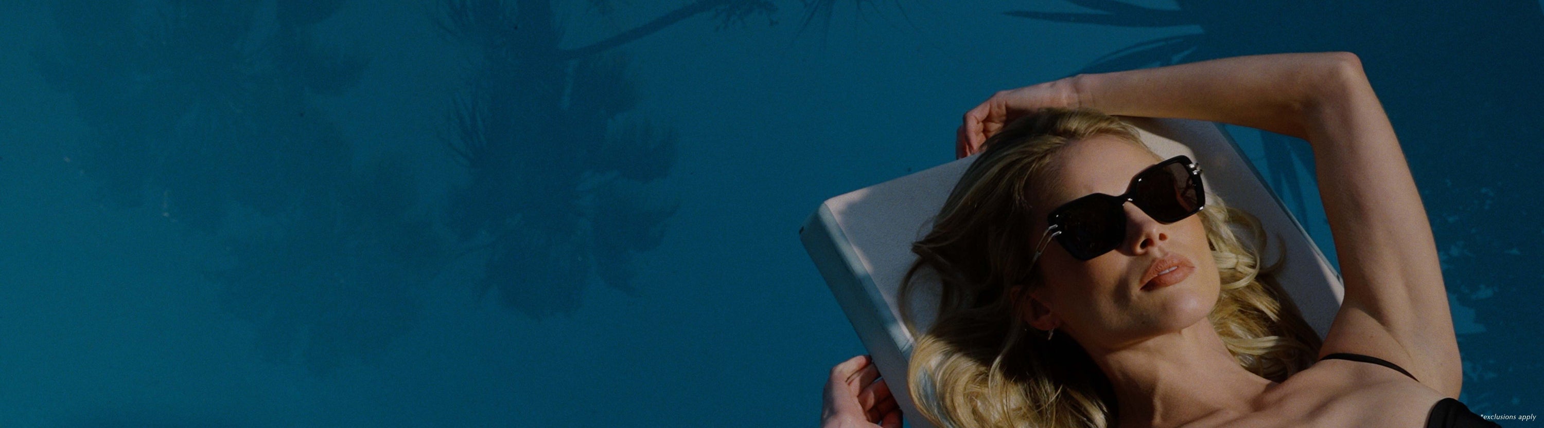 Blonde woman with black one piece and black oversized sunglasses poolside