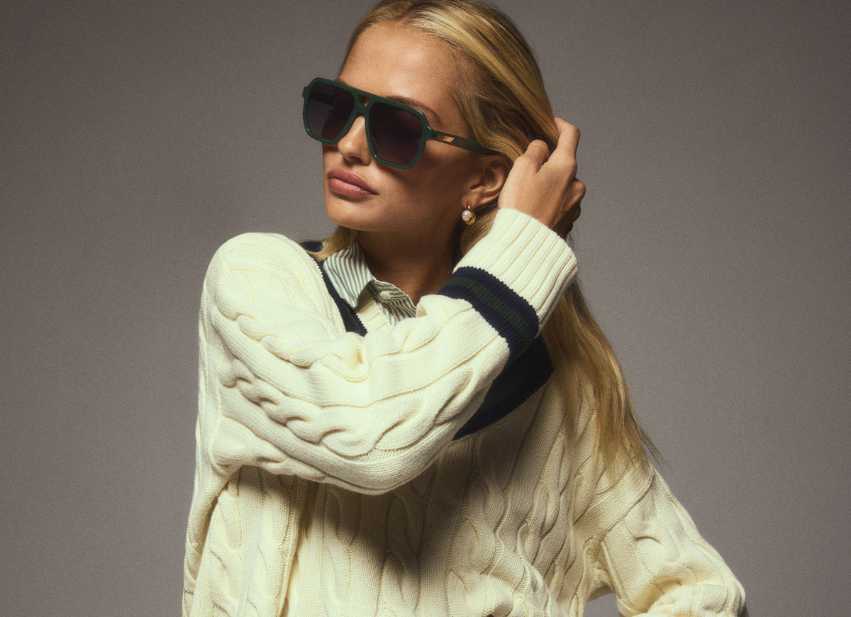 Studio shot of young woman pushing her hair behind her ear while wearing Cameran sunglasses