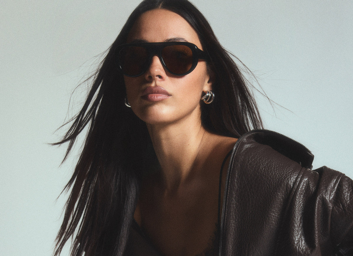 Studio shot of young woman wearing black leather jacket looking into camera wearing black Morgan sunglasses