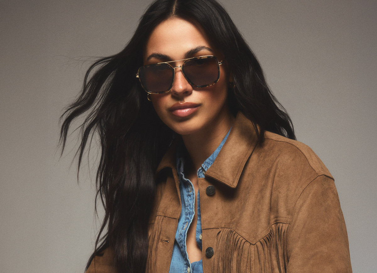 Studio shot of woman wearing Jordan tortoise-color framed sunglasses while wearing a suede leather jacket