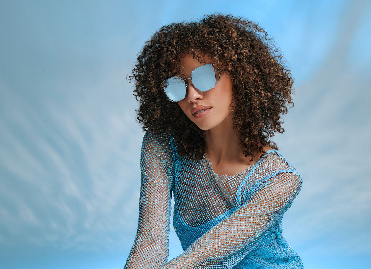 elsa disney princess model wearing blue mirrored oversized diff sunglasses with icy blue background