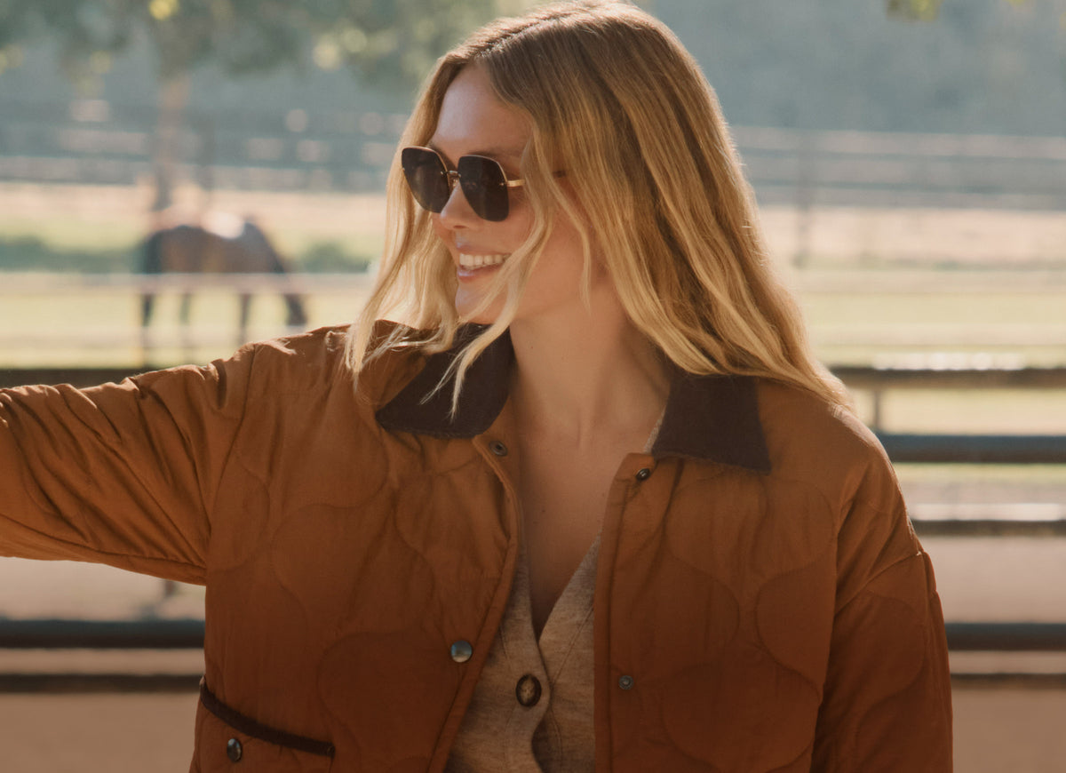 Blonde woman wearing oversized gold metal frame sunglasses with brown gradient lens in ranch western fashion