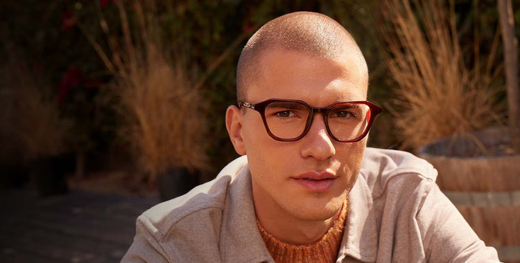 Male wearing chestnut crystal blue light glasses while sitting outside during golden hour in front of fall shrubbery