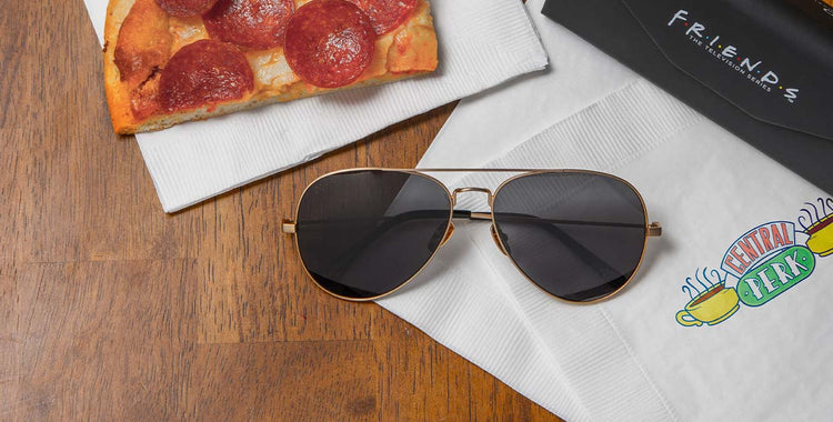 Flatlay of Friends How You Doin' Gold aviator sunglasses with grey lens on table on top of napkin from Central Perk