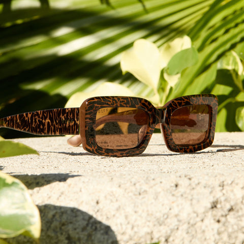 lifestyle - still life of diff eyewear indy rectangular sunglasses in a leopard tortoise frame laying outdoors