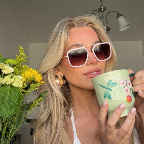 shelby hunstad blonde influencer wearing baby pink navigator sunglasses with pastel painted tea mug and spring flowers