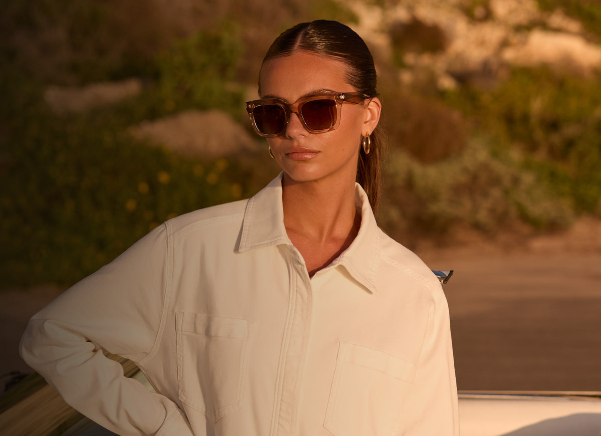 female wearing travis mathew x diff eyewear  Valencia in Soft Taupe Crystal strolling down the beach